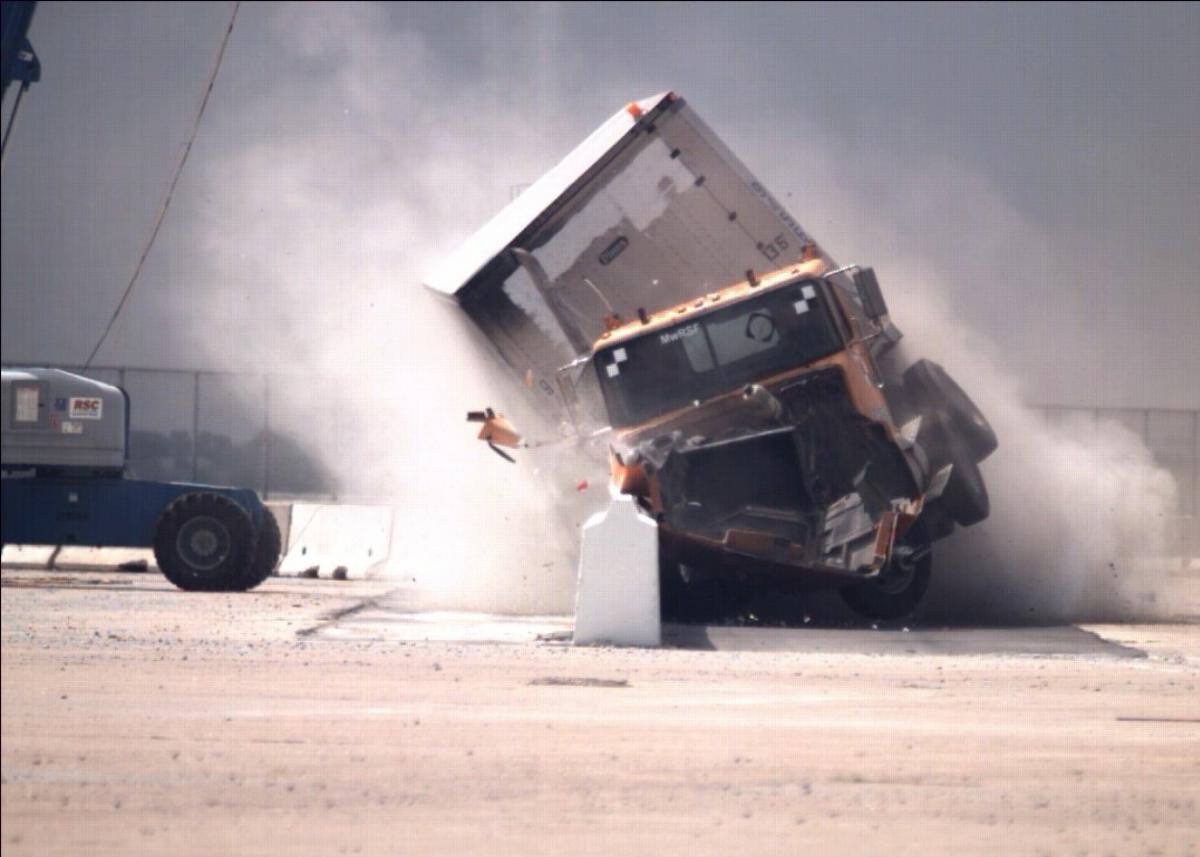 Semi-truck crashing into a concrete barrier sideways during a crash test.