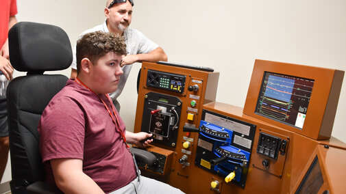 BNSF employee watching over a student as they operate a railroad locomotive simulator.