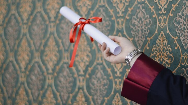 Hand holding a diploma rolled and tied with a red ribbon