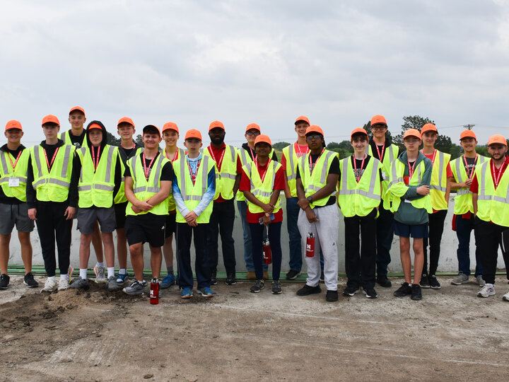 Group photo of all Discover Transportation Engineering students at a highway construction site in saftey vests and hats.