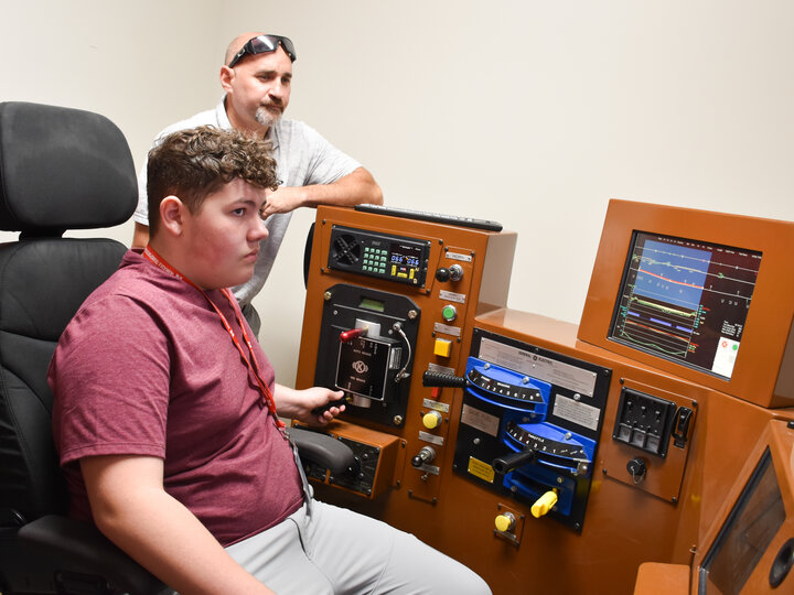 BNSF employee watching over a student as they operate a railroad locomotive simulator.