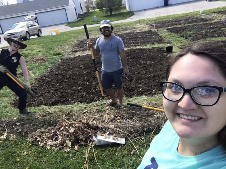 Rubi Quinones in front of a field with two other people holding shovels